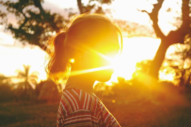 Foto retrato de una mujer de pie en el campo contra el sol brillante