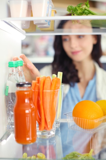 Retrato de mujer de pie cerca de una nevera abierta llena de alimentos saludables, verduras y frutas