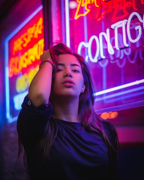 Foto retrato de una mujer de pie contra letreros de neón iluminados por la noche