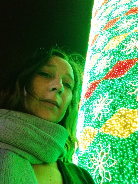 Foto retrato de una mujer de pie junto a una decoración de iluminación iluminada