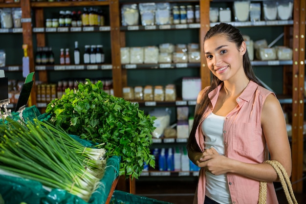 Foto retrato de mujer de pie junto a la pantalla de cebolletas y hierbas en la sección orgánica