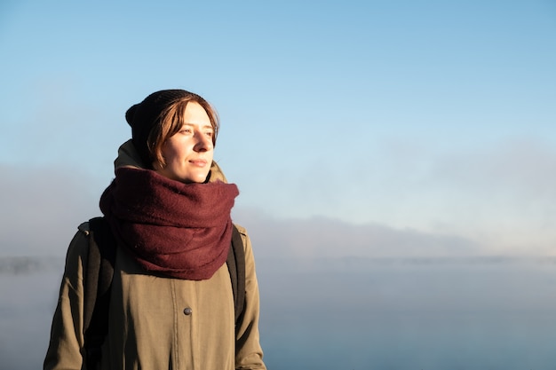 Retrato de mujer de pie en la luz del sol de la mañana. Excursionista femenina disfrutando del sol naciente en un hermoso fondo natural cubierto de niebla