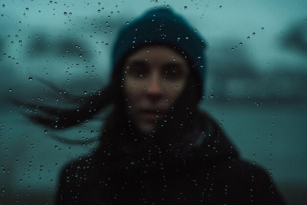 Retrato de una mujer de pie en una ventana de vidrio húmedo