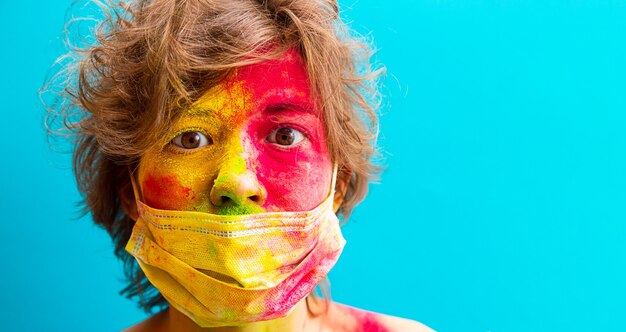 Foto retrato de una mujer en pintura holi de color seco y máscara protectora médica