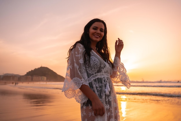 Retrato de una mujer en una playa al atardecer con un vestido blanco disfrutando del verano