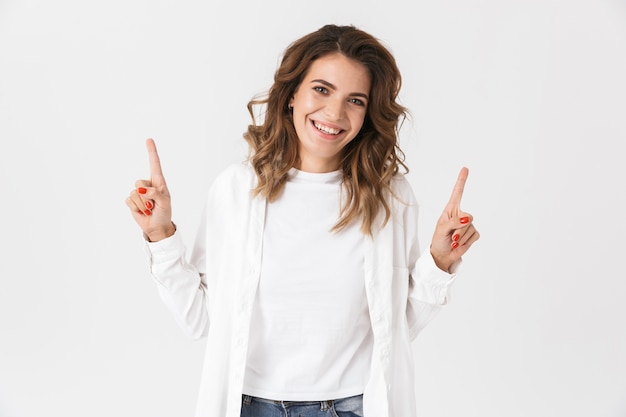 Retrato de mujer positiva en ropa casual apuntando con el dedo hacia arriba, aislado sobre blanco