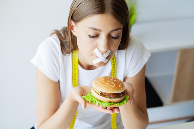 Retrato de una mujer que quiere comer una hamburguesa pero tiene la boca tapada