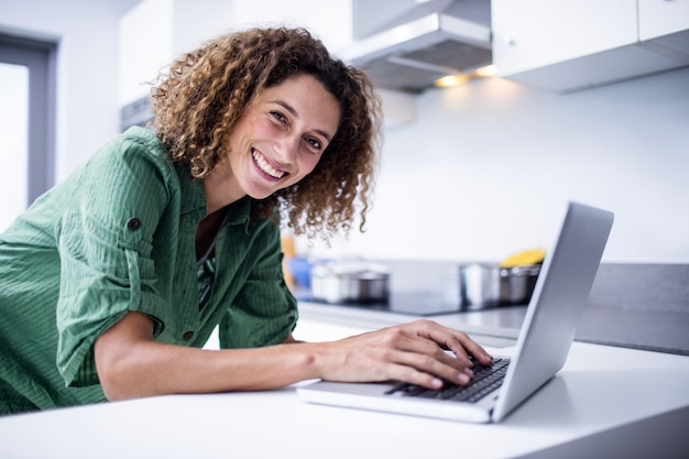 Retrato de mujer que trabaja en la computadora portátil en la cocina