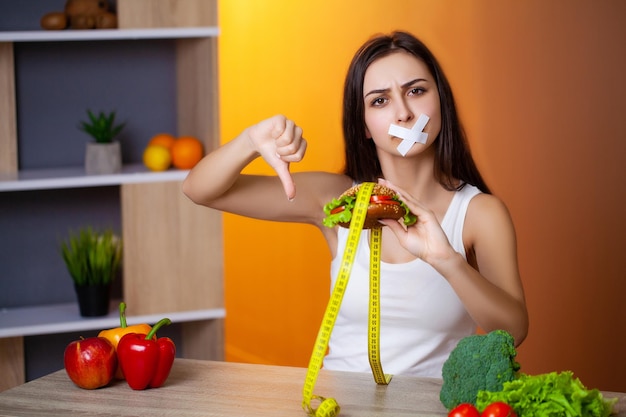 Retrato de mujer quiere comer una hamburguesa pero atascado boca de skochem, el concepto de dieta.