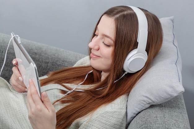 Retrato de una mujer relajada con auriculares sentada en un sofá y escuchando música en una tableta digital