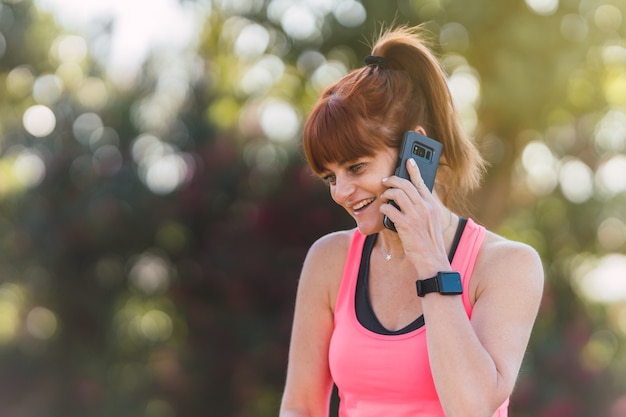 Retrato de una mujer en ropa deportiva hablando por un teléfono móvil en un parque.