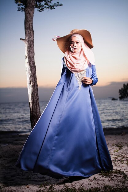 Foto retrato de una mujer con ropa y sombrero tradicionales de pie en la playa contra el cielo