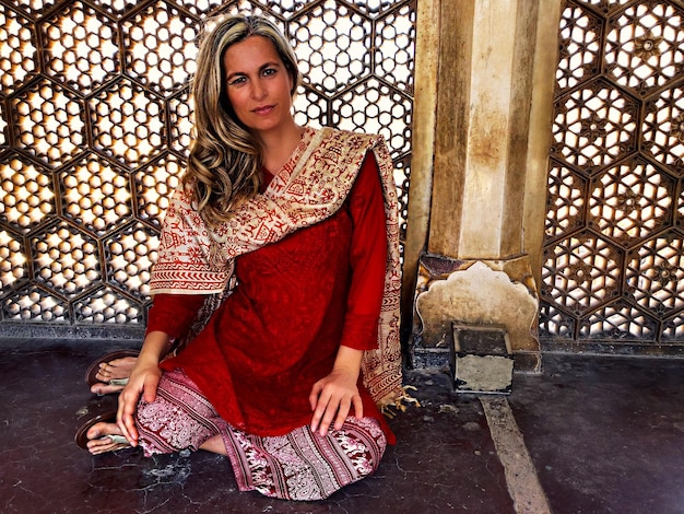 Foto retrato de una mujer con ropa tradicional mientras está sentada contra la pared