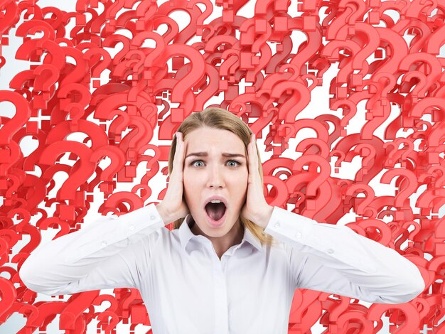 Retrato de una mujer rubia con una blusa blanca gritando aterrorizada contra un fondo hecho de signos de interrogación rojos.
