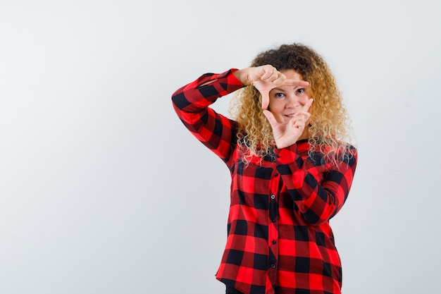 Retrato de mujer rubia con cabello rizado haciendo gesto de marco en camisa a cuadros y mirando jovial vista frontal