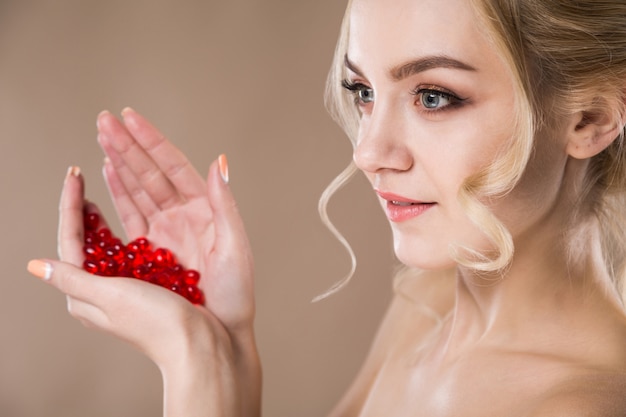 Retrato de una mujer rubia con cápsulas rojas de vitaminas en sus manos