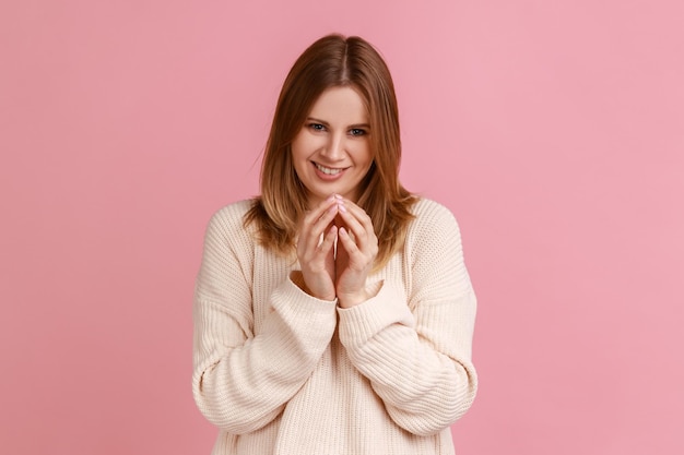 Retrato de mujer rubia intrigante pensando en un plan tortuoso con expresión de cara astuta, teniendo una idea astuta para bromear, usando suéter blanco. Disparo de estudio interior aislado sobre fondo rosa.