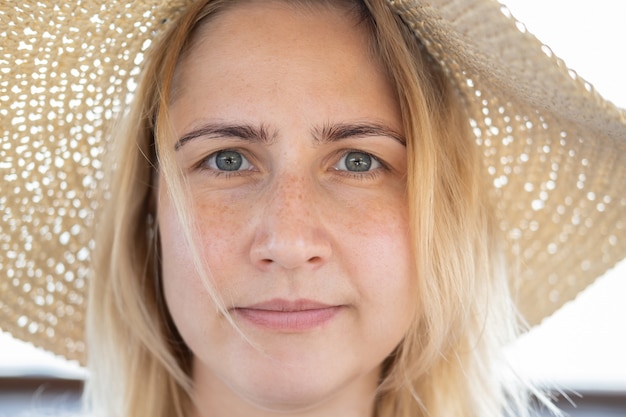 Retrato de mujer rubia joven atractiva con sombrero de paja con piel limpia y pecas.