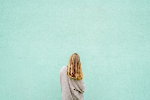 Retrato de mujer rubia de pie contra la pared azul. Vista trasera