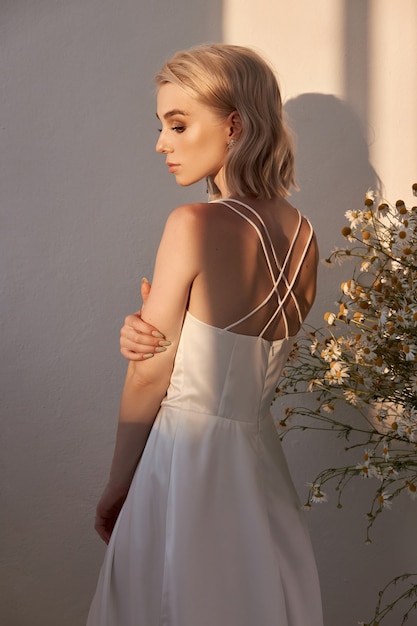 Retrato de una mujer rubia sexy con un hermoso vestido blanco en el sol de la tarde. Chica romántica con hermoso maquillaje natural