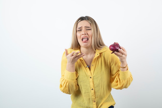 Retrato de mujer rubia sosteniendo cebolla roja con expresión de disgusto