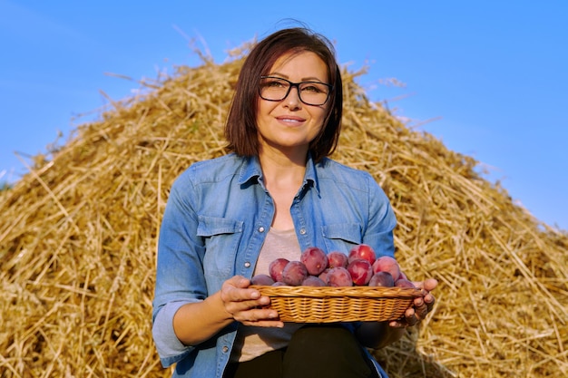 Retrato de mujer rural de verano con cesta de ciruelas fondo de cielo de heno seco