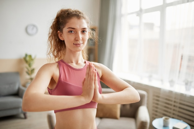 Retrato de mujer sana mirando al frente mientras está de pie y meditando en la habitación de su casa