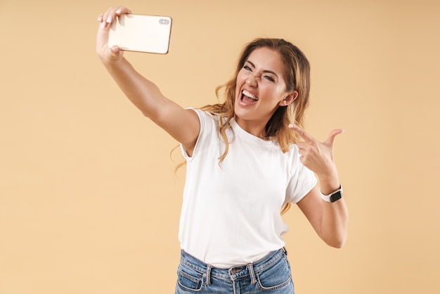 Retrato de mujer seductora sonriendo a la cámara mientras toma una foto selfie en el teléfono celular aislado