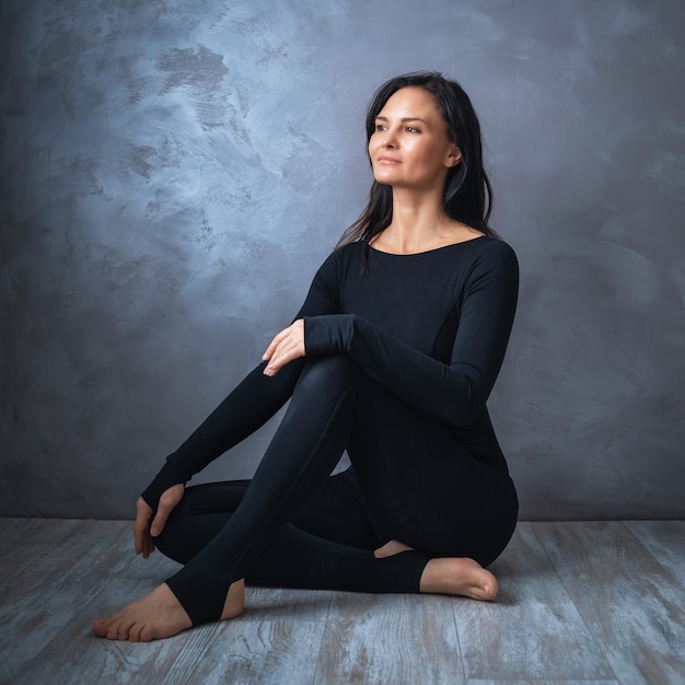 Retrato de una mujer segura sentada en un piso de madera con ropa deportiva en instructor de yoga negro