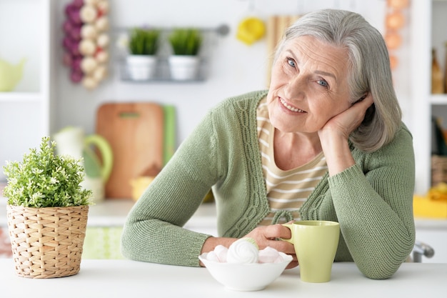 Retrato de mujer senior feliz en la mesa con taza de té