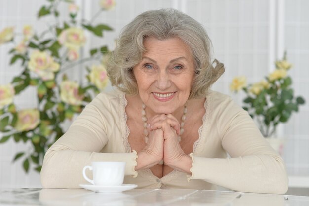 Retrato de mujer senior feliz en la mesa con taza de té