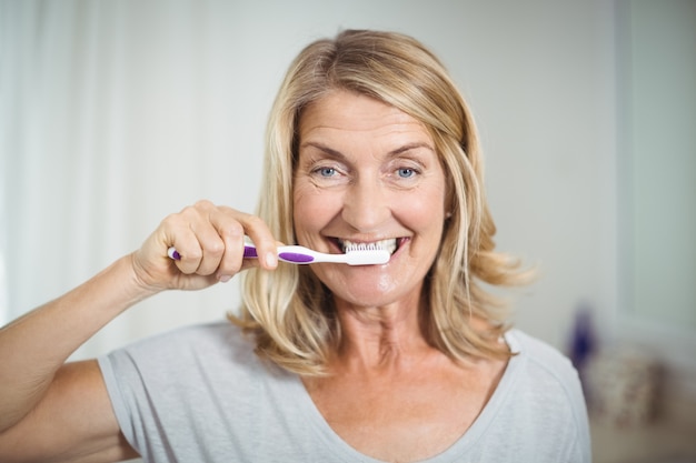 Retrato de mujer senior limpiándose los dientes en el baño.