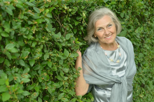 Retrato de mujer senior sonriente cerca de seto verde de verano