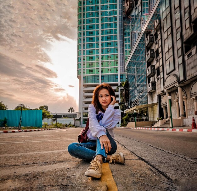 Foto retrato de una mujer sentada contra los edificios de la ciudad