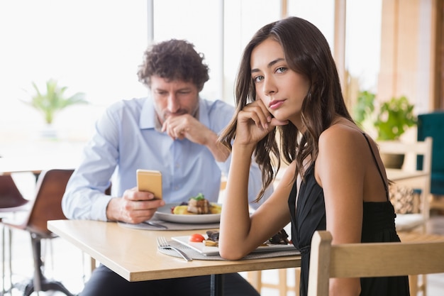 Retrato de mujer sentada mientras el hombre usando un teléfono móvil en segundo plano.