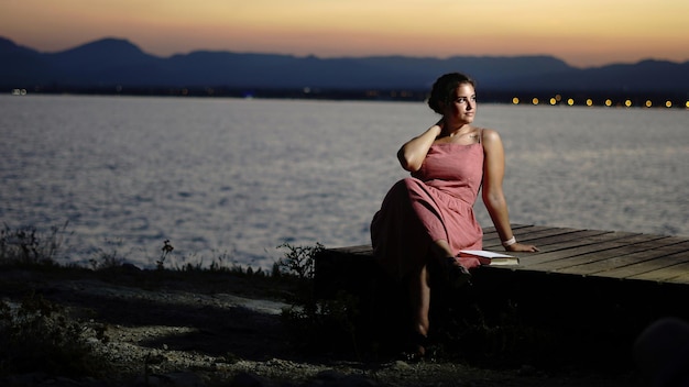 Foto retrato de una mujer sentada en la orilla contra el cielo durante la puesta de sol