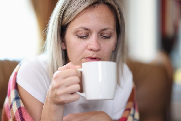 Retrato de mujer sentada en un sofá envuelto en una manta y bebiendo té temporada de otoño frío y