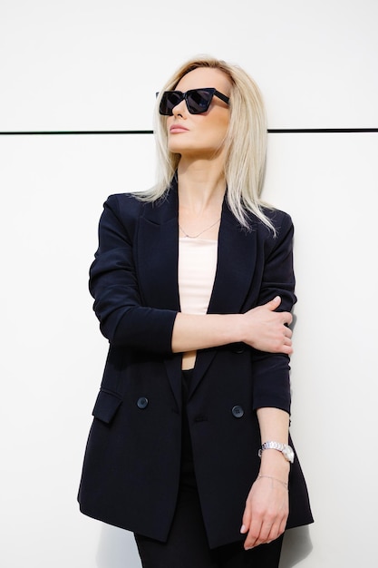 Retrato de una mujer sexy y elegante de pie en la calle con traje negro y gafas de sol en un soleado día de primavera