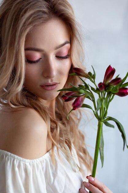 Retrato de una mujer sexy y encantadora con una blusa blanca con una flor en las manos