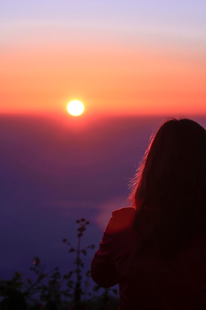 Foto retrato de una mujer en silueta contra un cielo naranja durante la puesta de sol