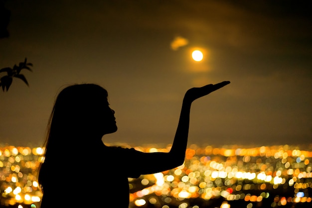 Retrato de mujer de silueta con luna llena en la noche de la ciudad de luz de fondo bokeh