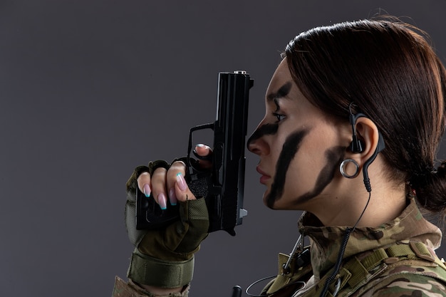 Retrato de mujer soldado en uniforme militar con pistola en la pared oscura