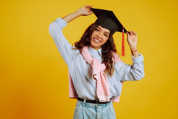 Retrato de mujer con un sombrero de graduación en la cabeza posando en amarillo.