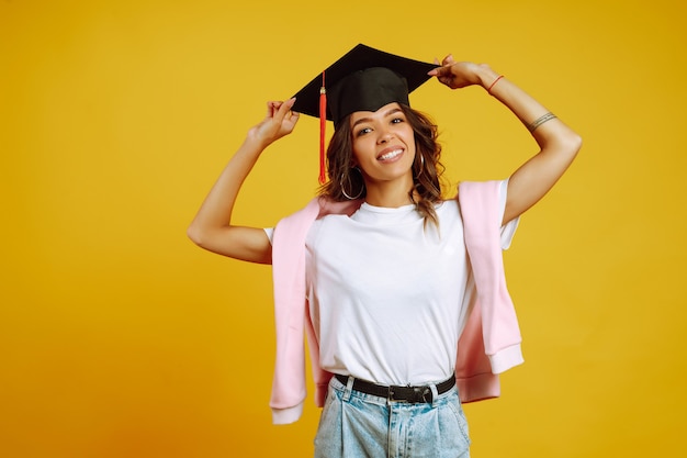 Retrato de mujer con un sombrero de graduación en la cabeza posando en amarillo.