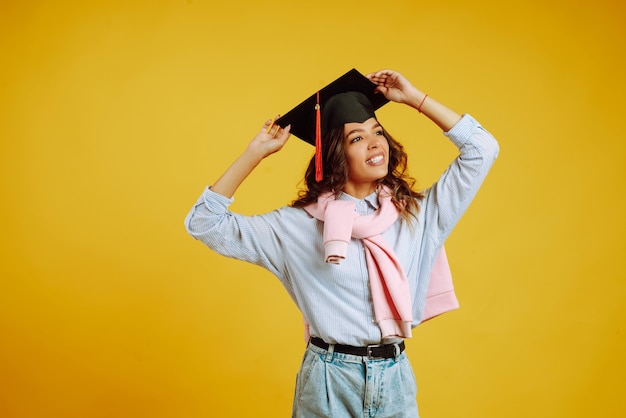 Retrato de mujer con un sombrero de graduación en la cabeza posando en amarillo.