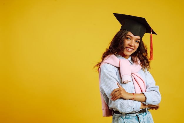 Retrato de mujer con un sombrero de graduación en la cabeza posando en amarillo.