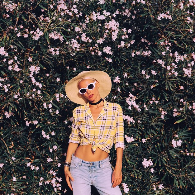 Foto retrato de una mujer con sombrero de pie contra las plantas con flores