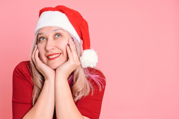 Retrato de una mujer soñando con un gorro de Papá Noel rojo sobre un fondo rosa