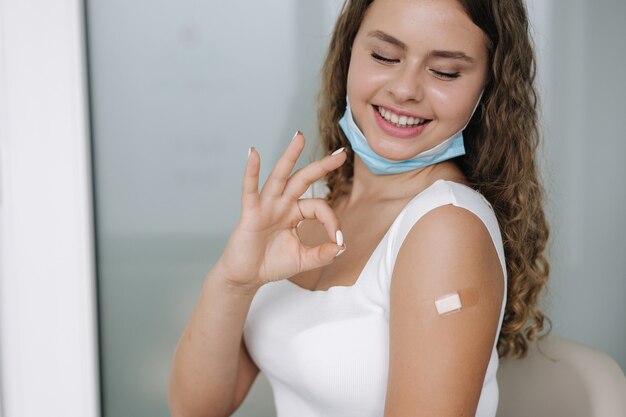 Retrato de una mujer sonriendo después de recibir la vacuna covid mujer dando un signo de mano ok y mostrándola