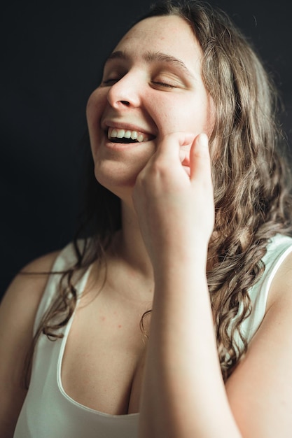 Retrato de una mujer sonriendo y llevándose la mano a la cara posando en un estudio con fondo negro Adulto joven aplica mascarilla facial nutritiva de cuidado diario en su piel